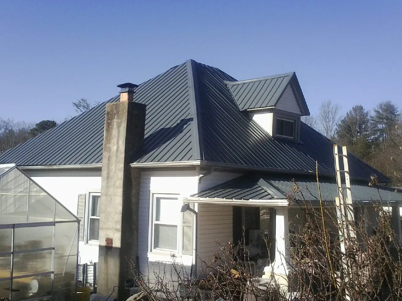 Dark blue standing seam metal roof on a white farmhouse with dormer — Slate & Tile Roof Repair by Roofing Brothers in Swanzey