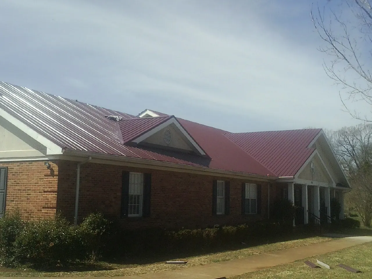 Red metal roof with gabled entries on a long brick building, from a Hail Damage Roof Repair job in Swanzey