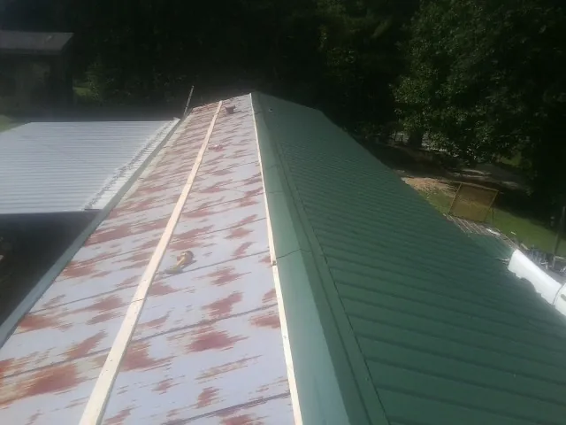 Old rusted panels beside newly installed green metal roofing — Wind Damage Roof Repair by Roofing Brothers in Swanzey