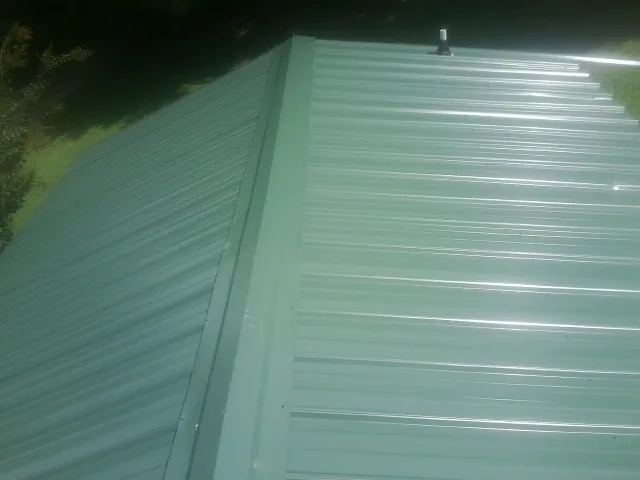 New green metal panels meeting at the ridge of a roof — Flat Roof Repair work by our crew in Swanzey