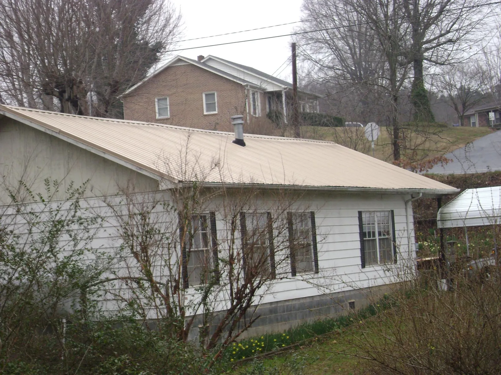 Tan metal roof on a white sided house set into a hillside — Commercial Roofing by Roofing Brothers in Swanzey