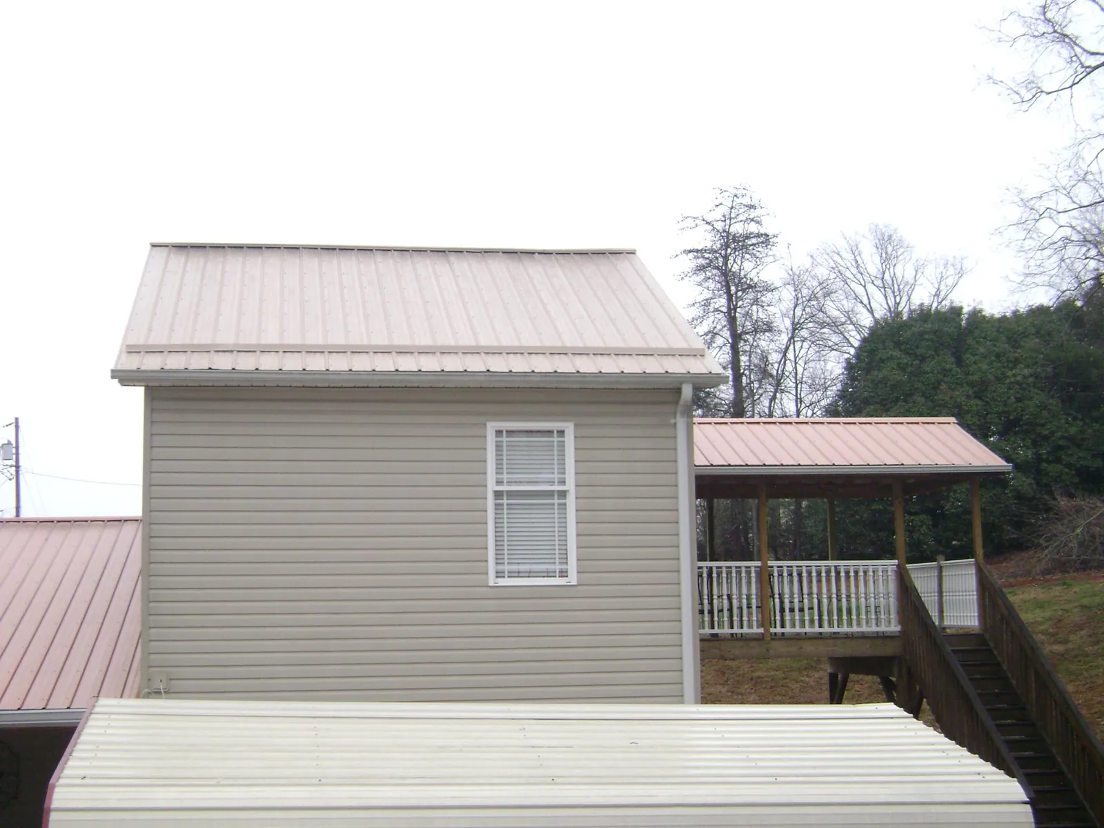 Tan metal roofs on a two story addition and attached porch, from a Roof Replacement job in Swanzey